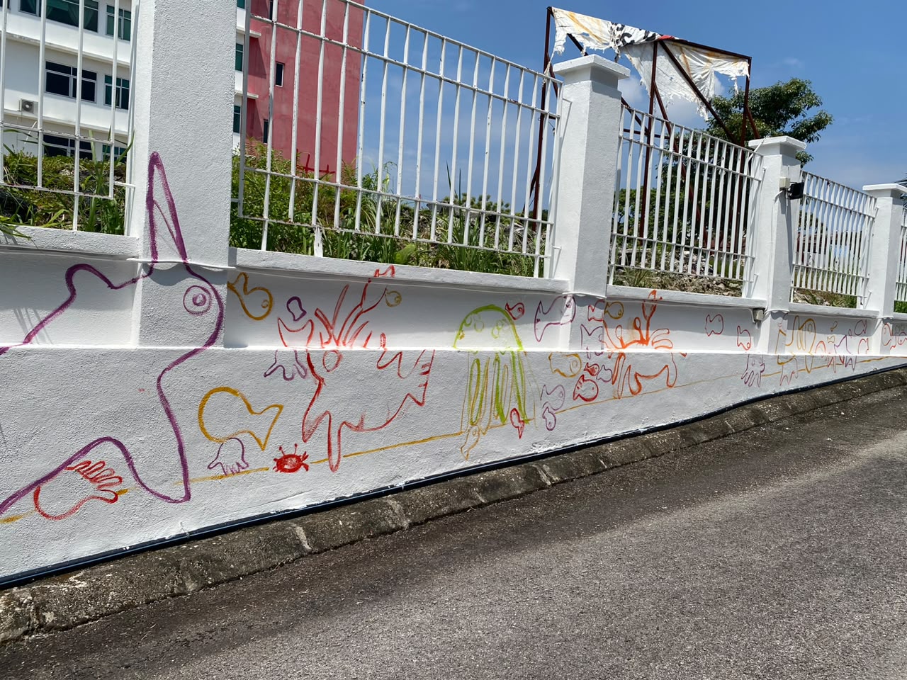 The freshly repainted white wall with the Celebrate the Beauty of Innocence mural taking shape in colourful painted outlines of fish, flowers and birds.